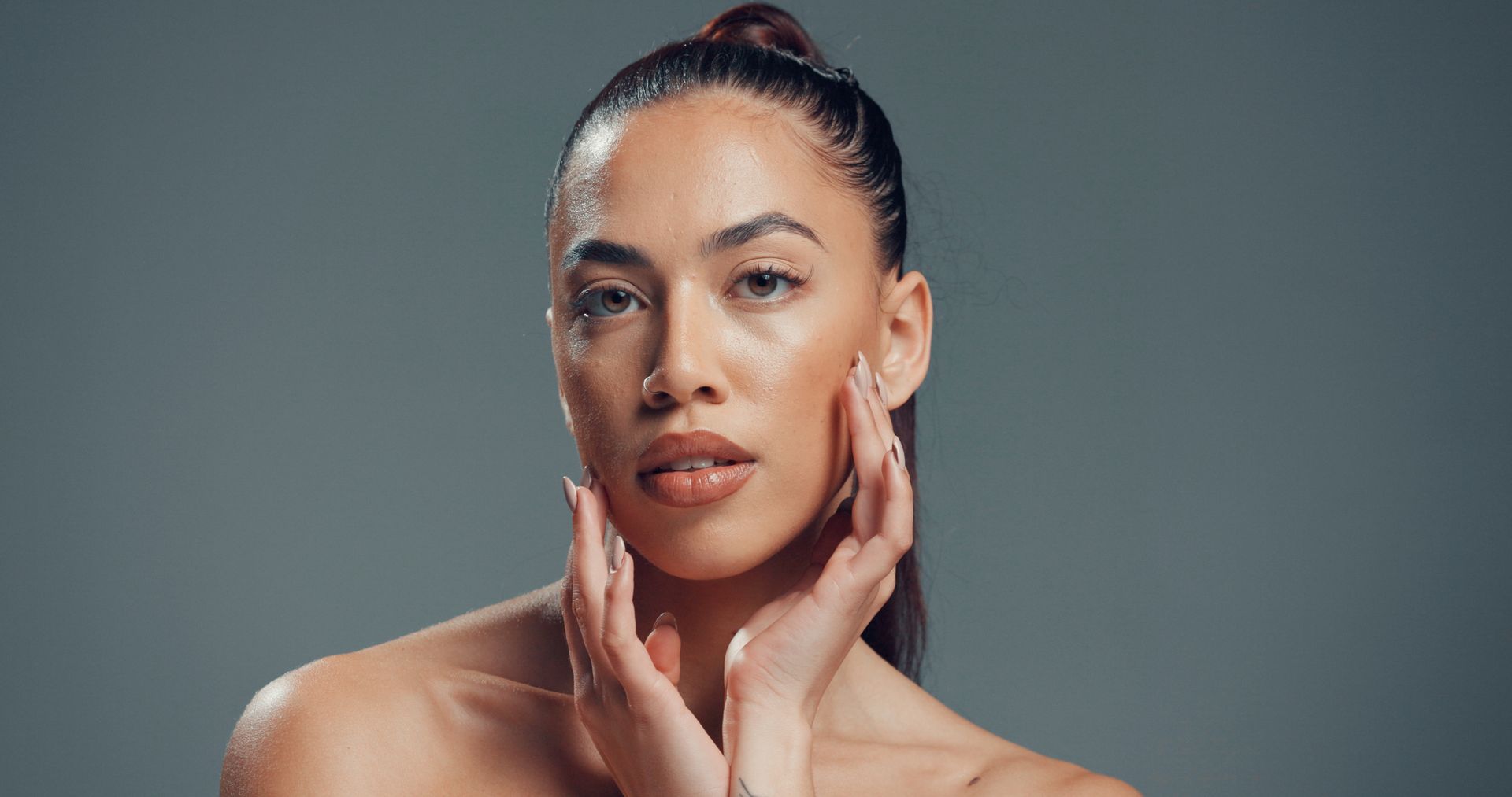 Portrait of a woman with hair in a bun, gently touching her face against a gray background