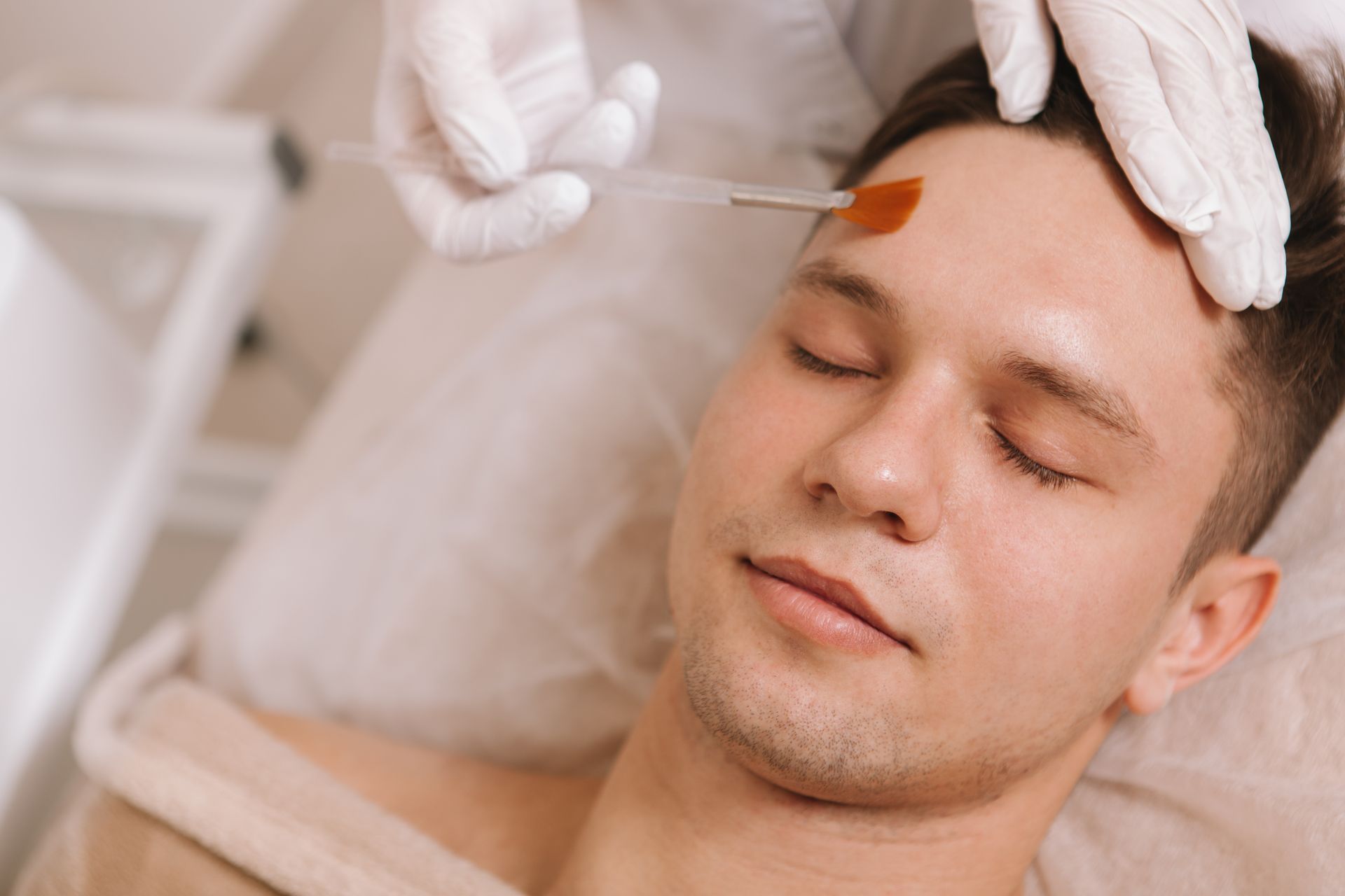 A person receiving a forehead treatment with a brush in a spa setting, eyes closed and relaxed.