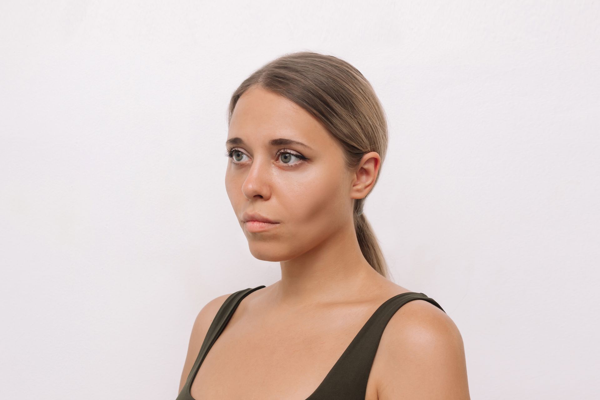 Woman with light skin, in a dark green tank top, looking off to the side, against a white background.