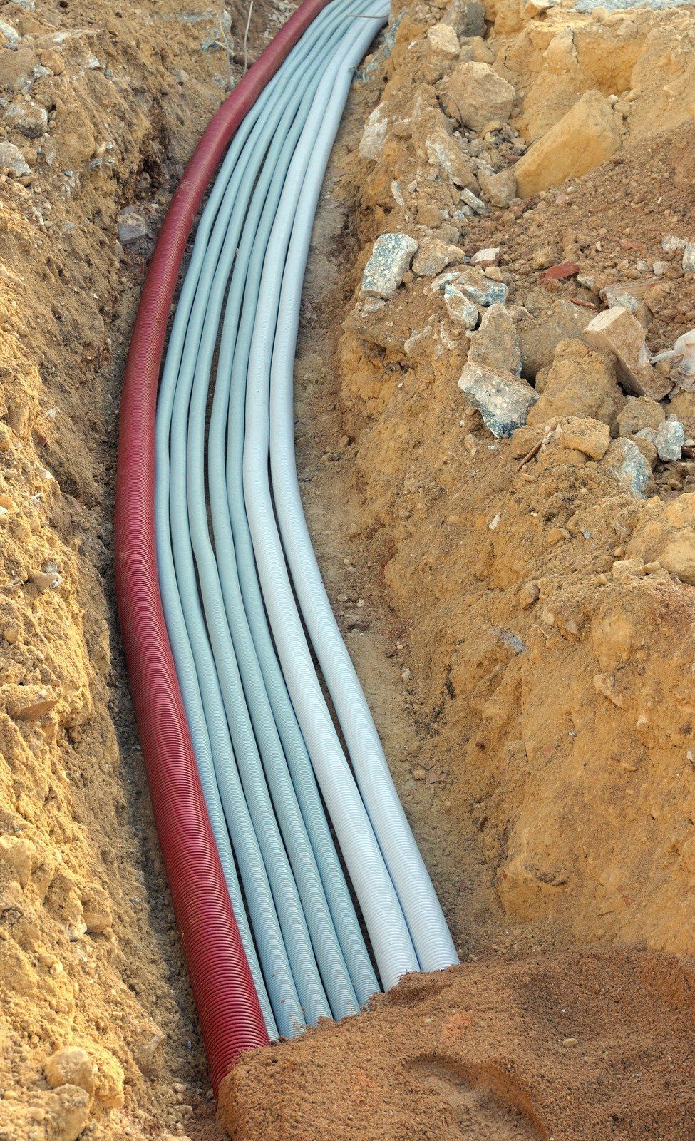 Trench with gray and red corrugated conduits laid in the earth.