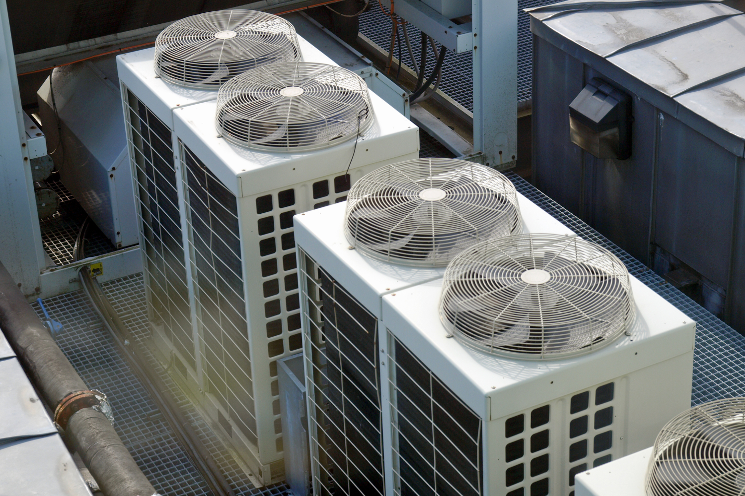 Rooftop view of several white air conditioning units with protective fan cages.