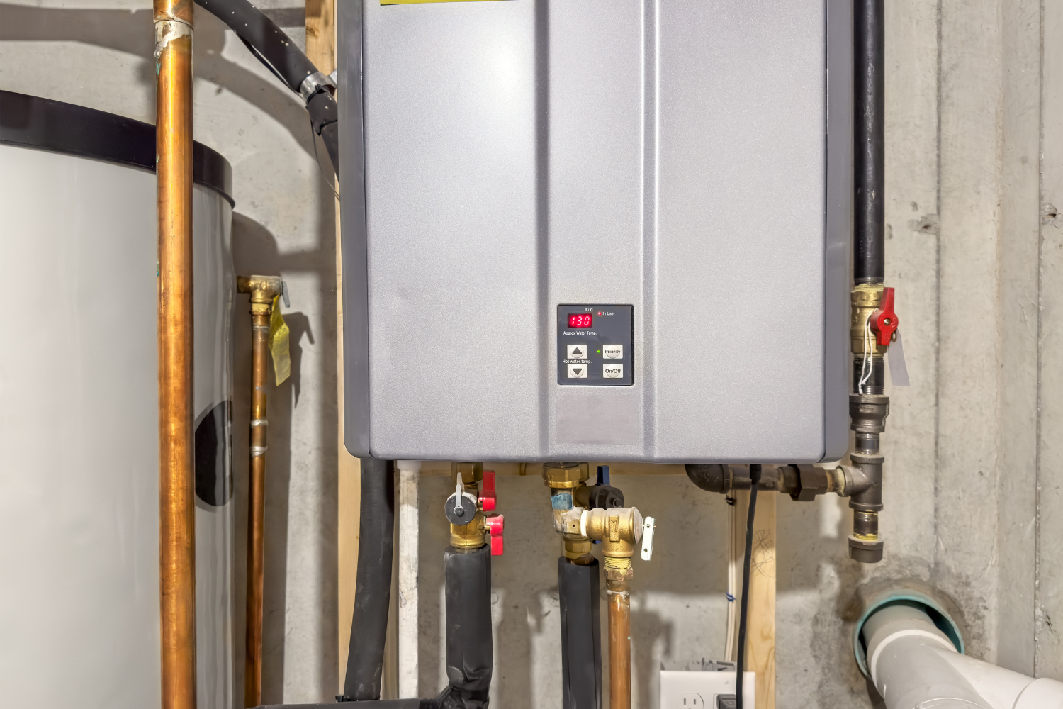 Tankless water heater installed on a basement wall with connected pipes and valves.