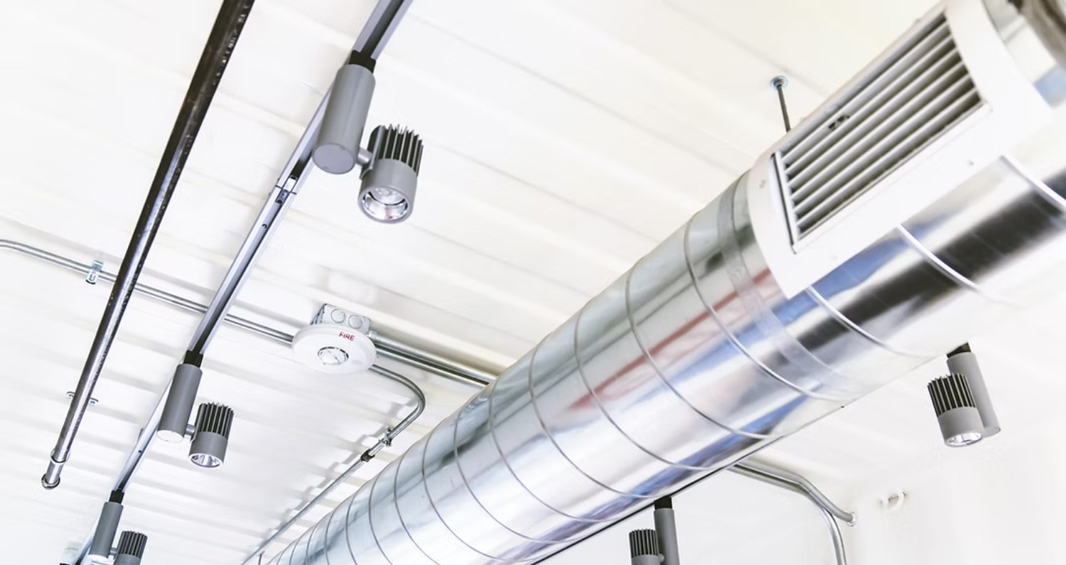 Metallic HVAC ductwork and track lighting on a white ceiling.