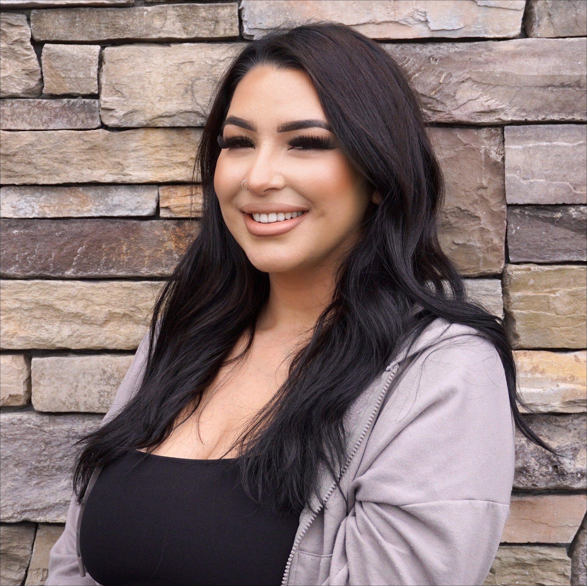 A woman is smiling in front of a stone wall.