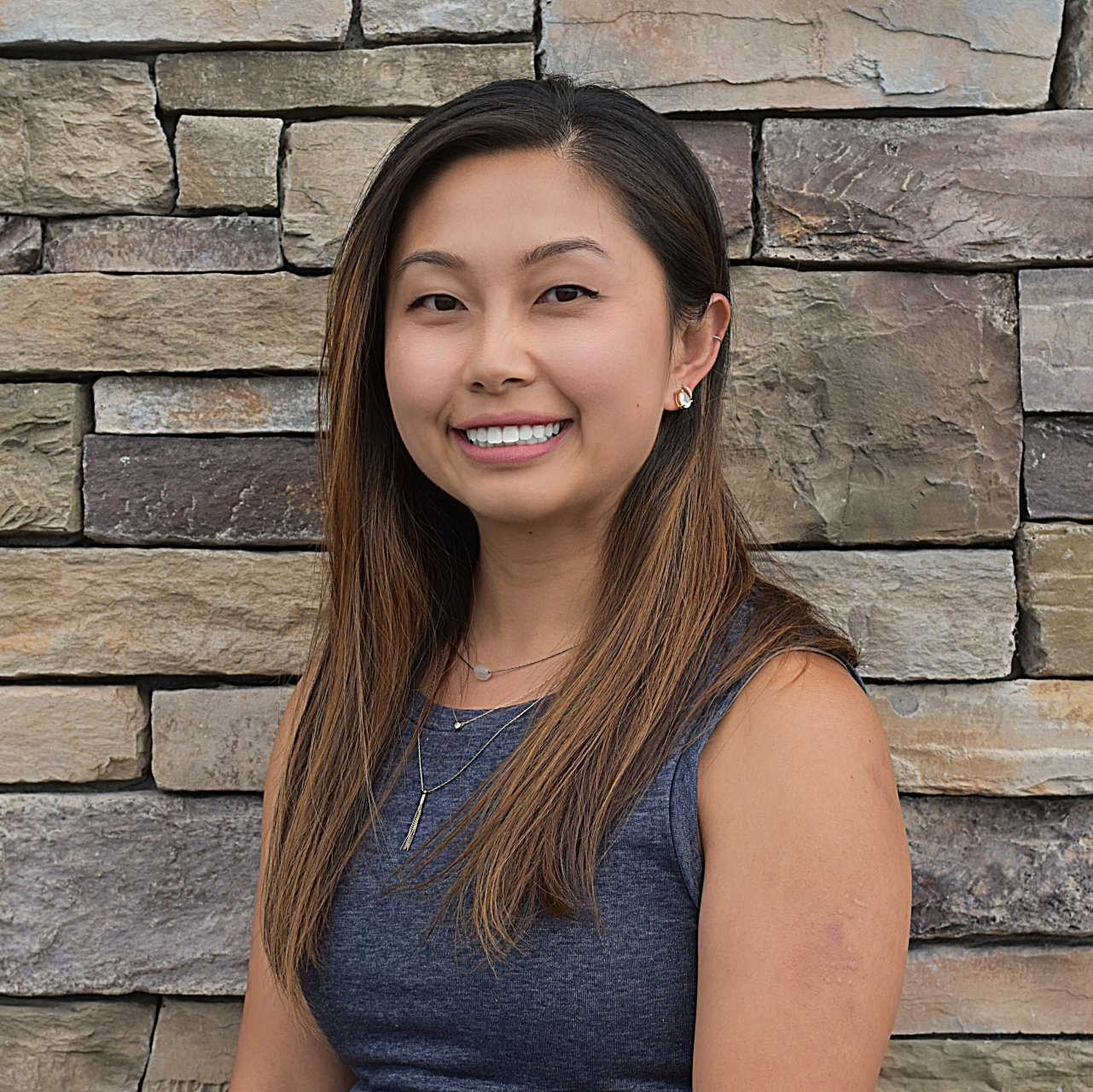 A woman is smiling in front of a stone wall.