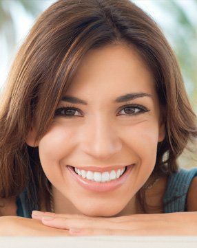 A woman is smiling with her hands on her face.