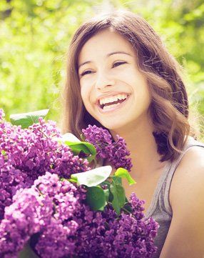 A woman is holding a bouquet of purple flowers and smiling.