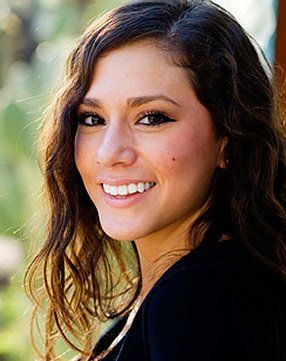 A woman with long curly hair is smiling for the camera.