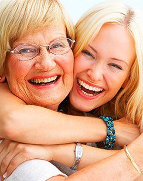 An older woman and a younger woman are hugging each other and smiling.