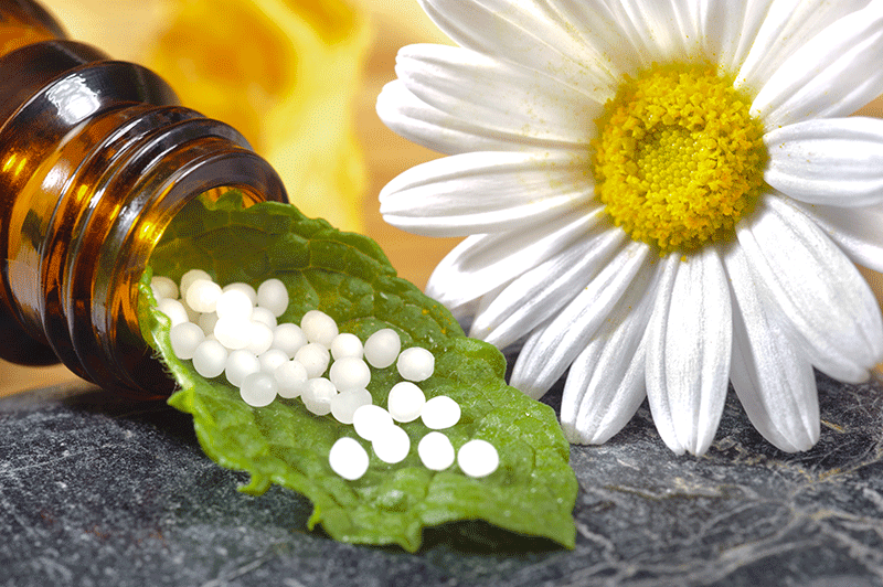 Eine Flasche Homöopathie neben einem Gänseblümchen und einem Blatt.