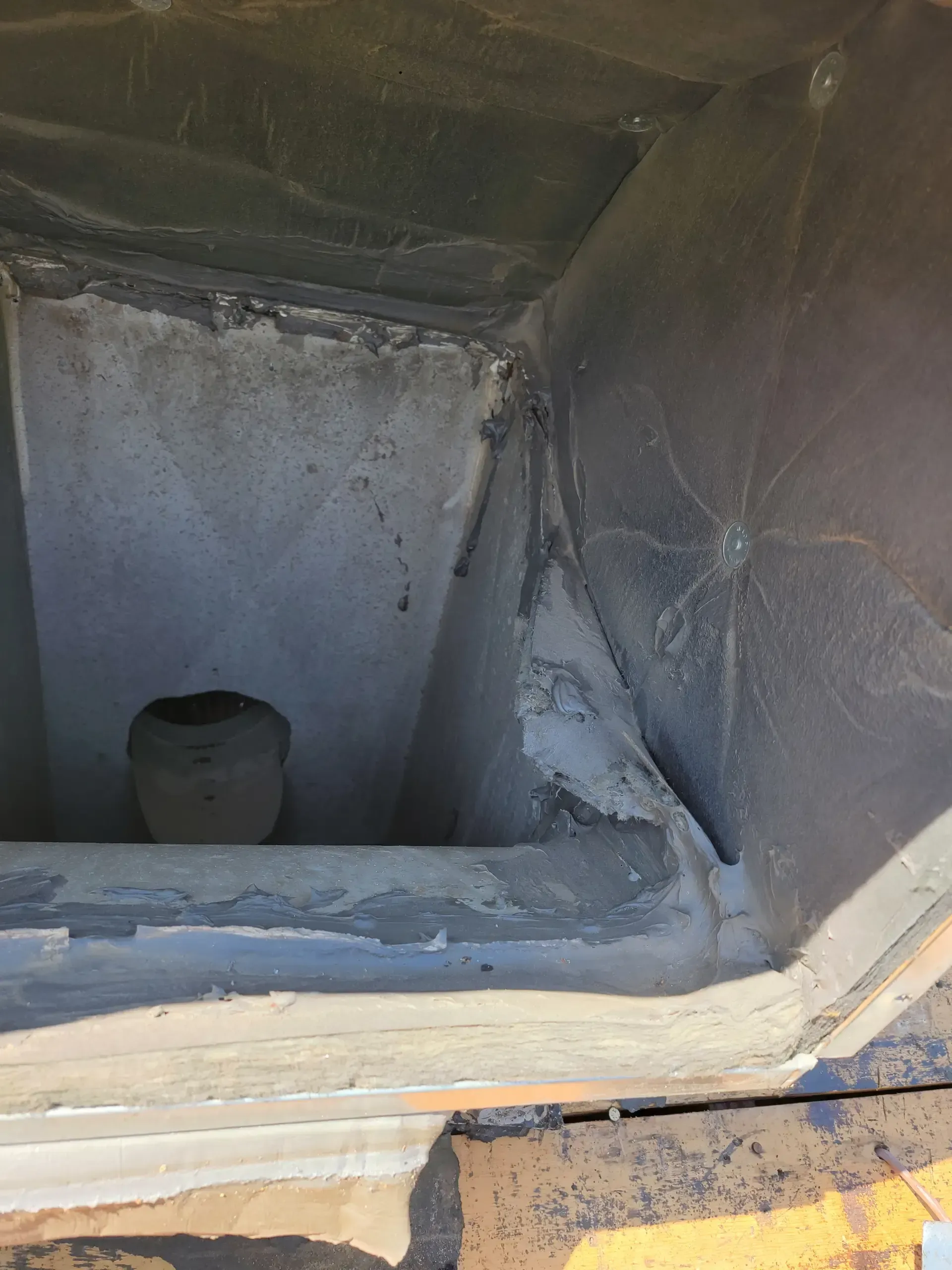 A top-down view into a square chimney flue showing rough gray concrete walls and a dark opening at the bottom.