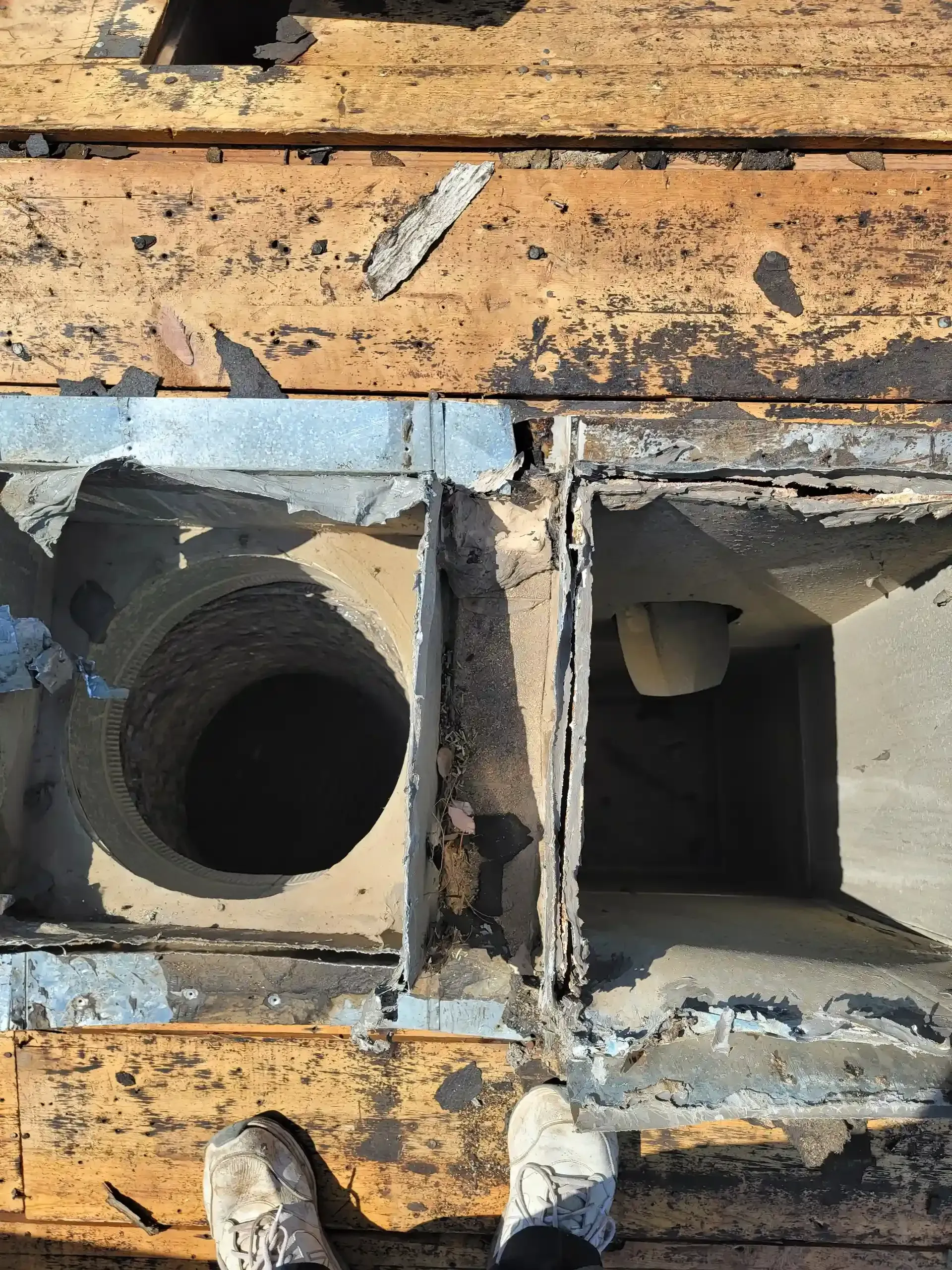 Top-down view of two chimney flues emerging from a roof, with a person's shoes visible at the bottom.
