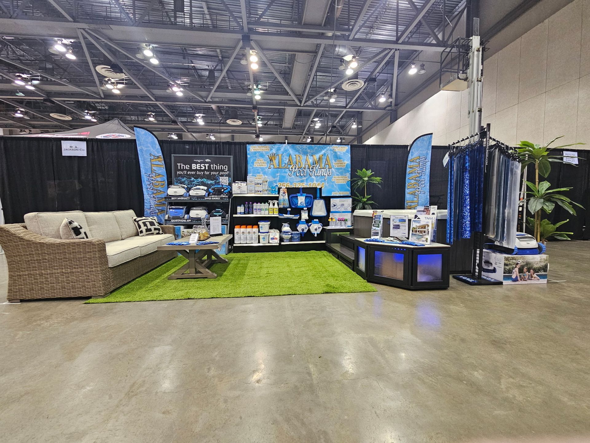 Booth display with pet products, green turf, and black-lit aquariums in a large convention hall.