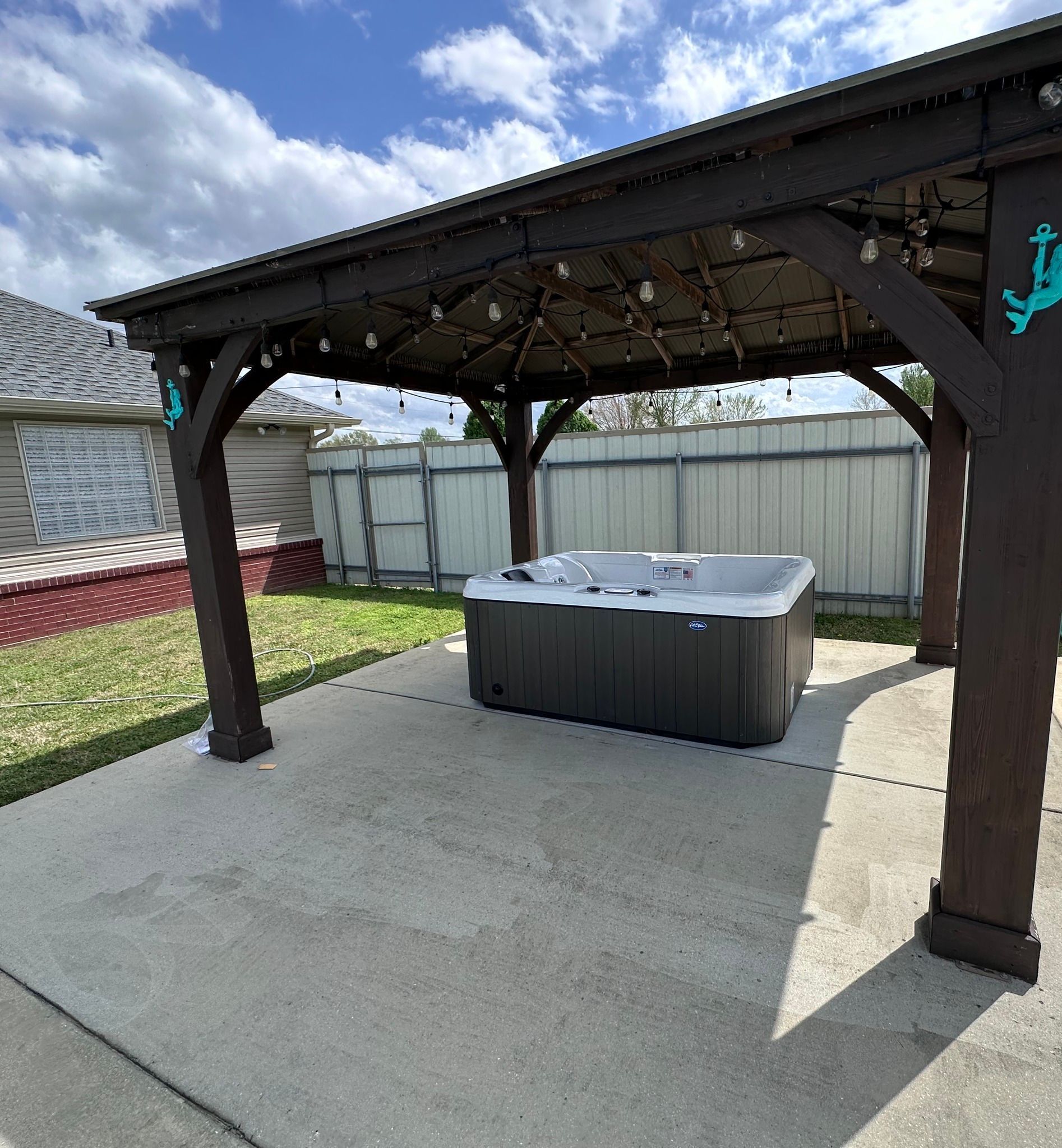 Backyard patio with a covered wooden pergola and a hot tub on a concrete slab.