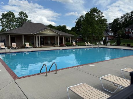 Outdoor swimming pool with lounge chairs and a clubhouse under a partly cloudy sky