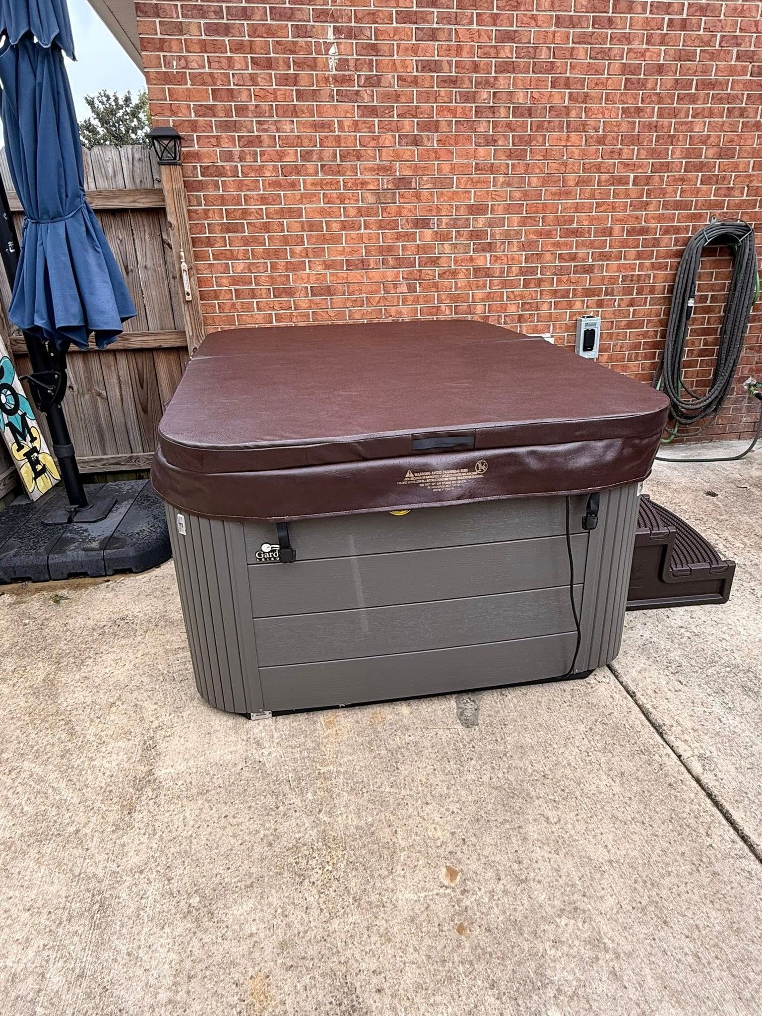 Closed brown hot tub against a brick wall on a concrete patio