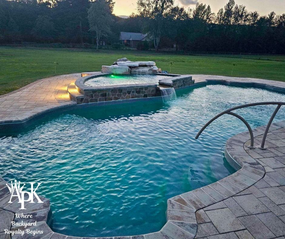 Backyard pool with a curved hot tub, turquoise water, and stone patio at dusk