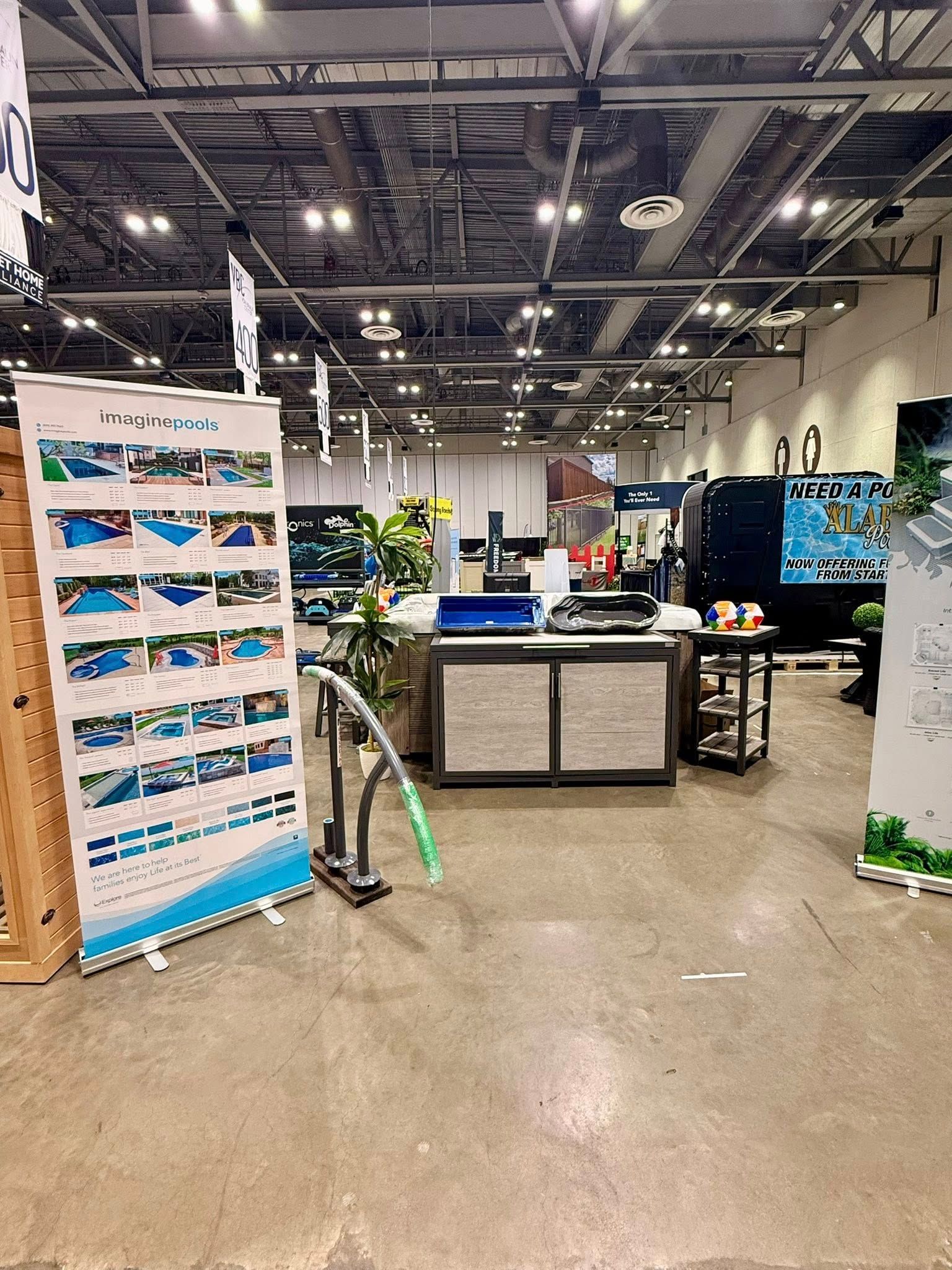 Indoor trade show booth with display panels, tables, and equipment under bright convention hall lights