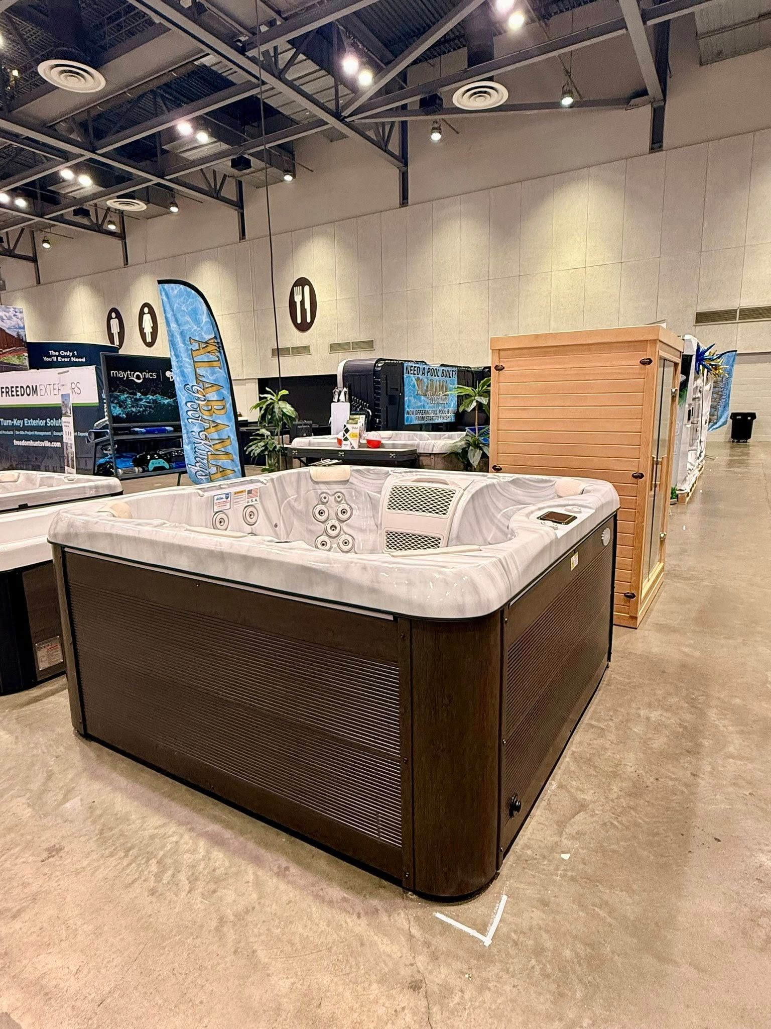 Hot tub display at an indoor showroom, with a brown spa and white interior under bright ceiling lights.