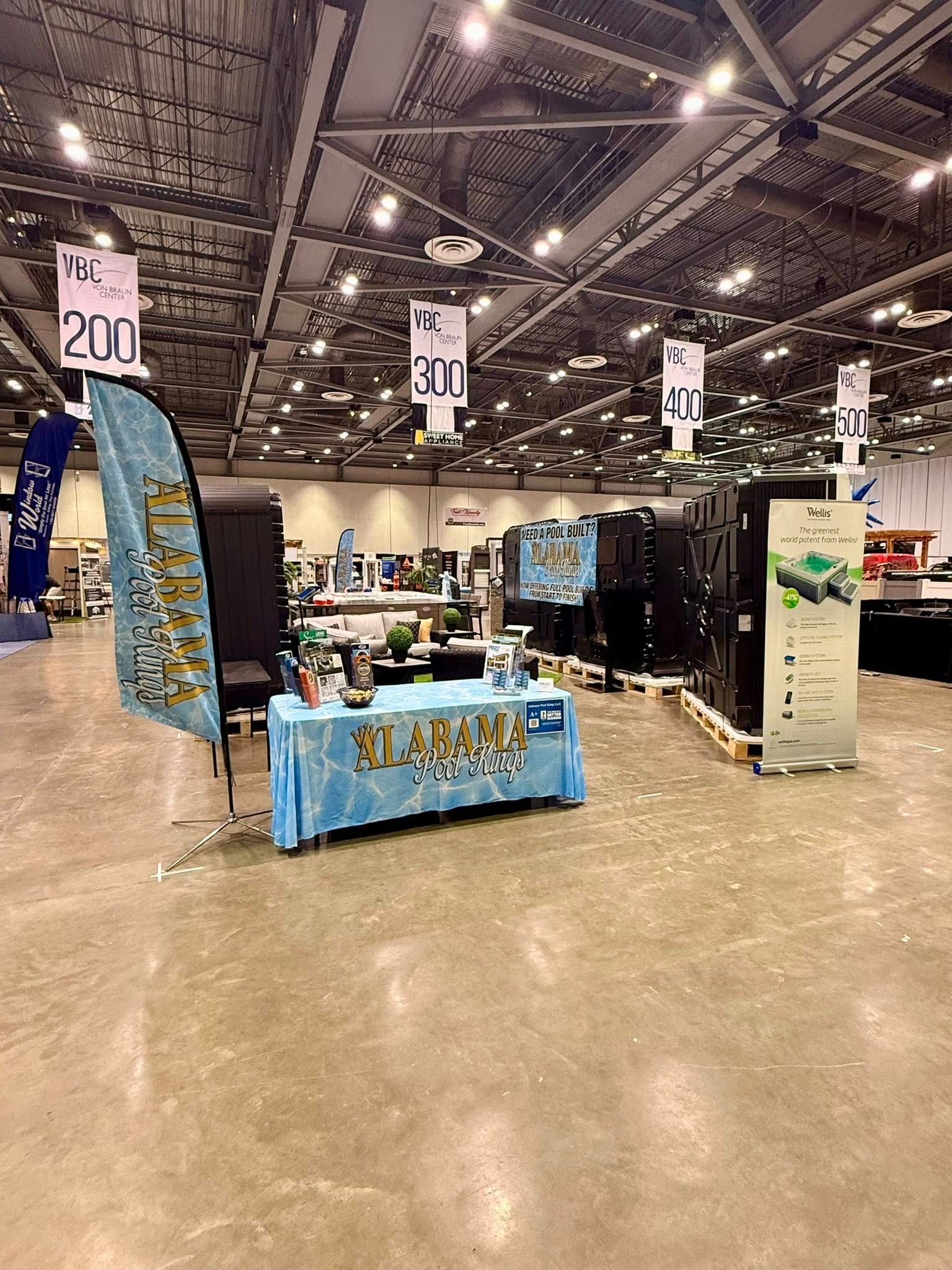 Booth display in a convention hall with blue tablecloths, signs, and a stone pillar exhibit.
