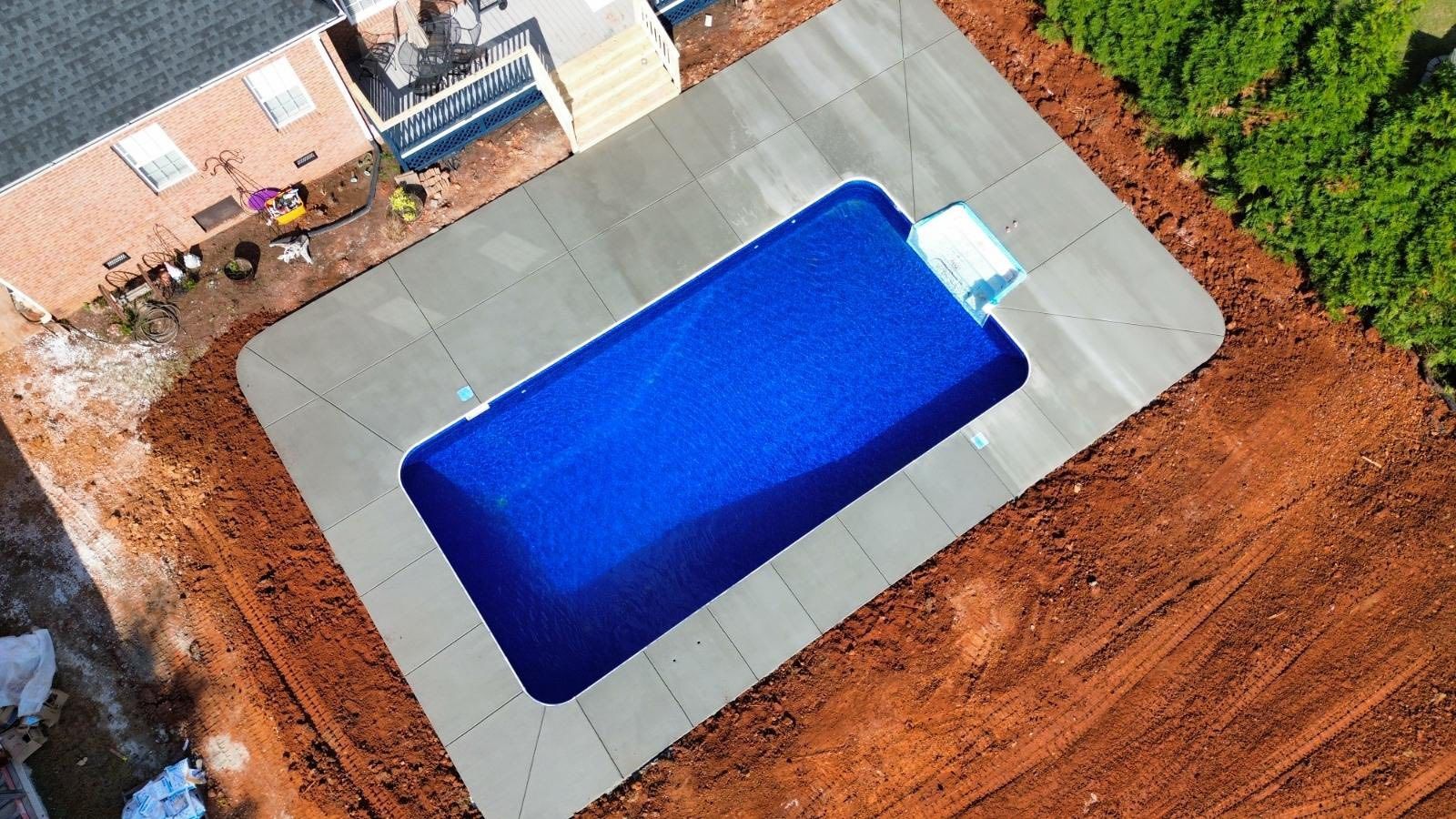 Aerial view of a backyard with a rectangular blue swimming pool surrounded by a concrete patio.