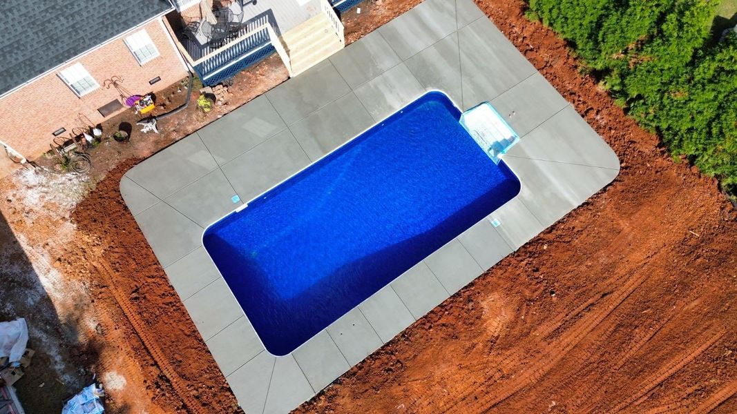 Aerial view of a backyard with a rectangular blue swimming pool and gray patio surround