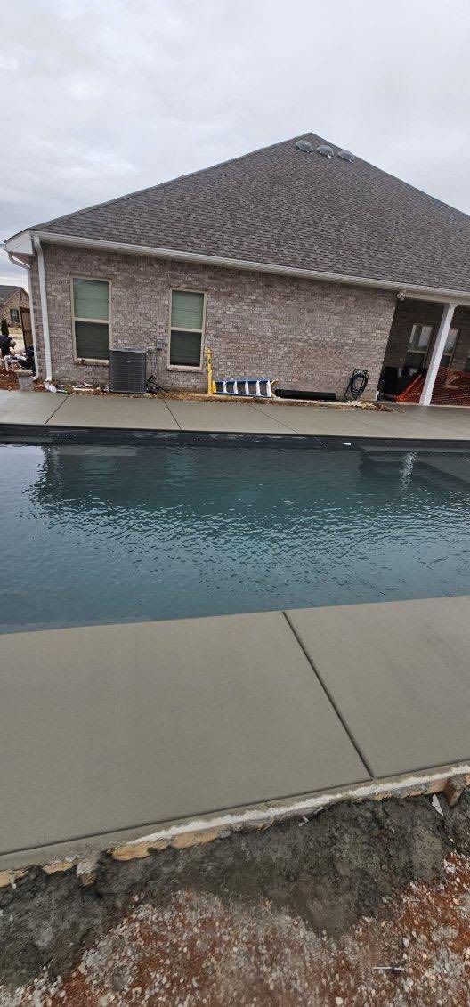 Backyard swimming pool beside a brick house under a cloudy sky