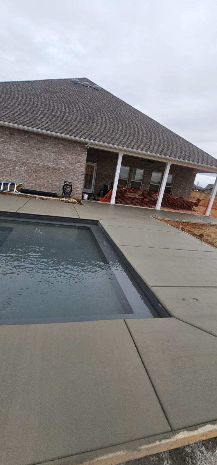 Backyard pool beside a brick house with a covered patio and tiled roof under a gray sky