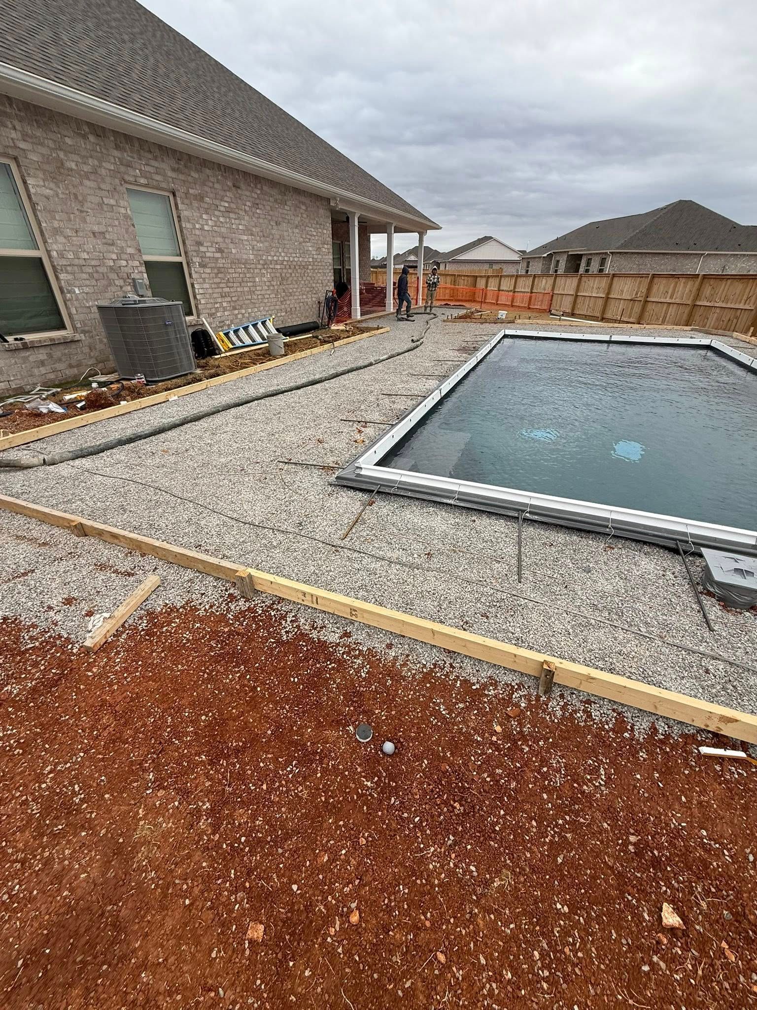Backyard under construction with gravel, red soil, a house, and an in-ground pool under cloudy skies