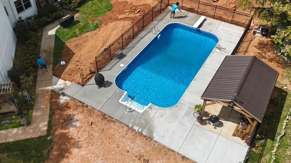Aerial view of a backyard pool under construction with blue liner, concrete deck, and a small shed nearby