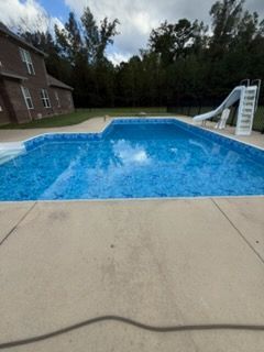 Backyard swimming pool with a white slide beside a brick house and concrete patio