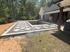 Backyard patio with a concrete pool deck and geometric white inlays beside a house and trees