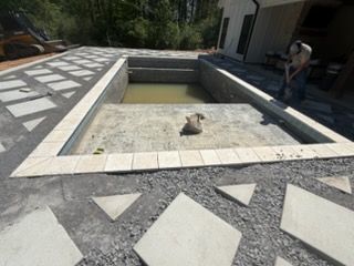 Concrete backyard pool with a person working on the patio area nearby
