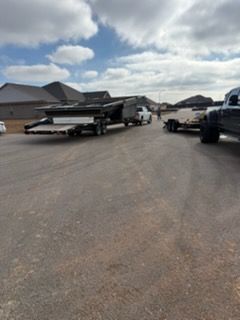 Parking lot with a black flatbed truck and trailer beside houses under a cloudy sky