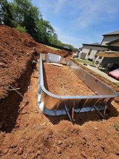 Foundation excavation with a metal form for a concrete slab beside a house on a sunny day