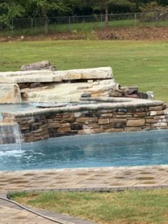 Backyard pool with stone waterfall and green lawn surrounding it