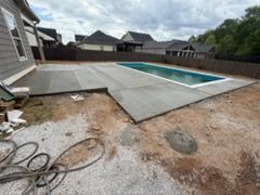 Backyard patio under construction beside a swimming pool, with concrete slabs and dirt