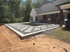 Construction crew installing a large geometric patio or deck beside a house in a wooded yard