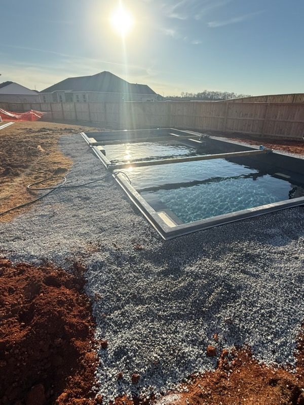 Backyard pool foundation with two water-filled rectangular sections at sunset, surrounded by gravel and fencing