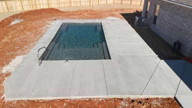 Backyard swimming pool with a concrete patio and dirt landscaping around it