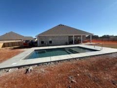 Backyard with a rectangular in-ground pool beside a new single-story house under a clear blue sky