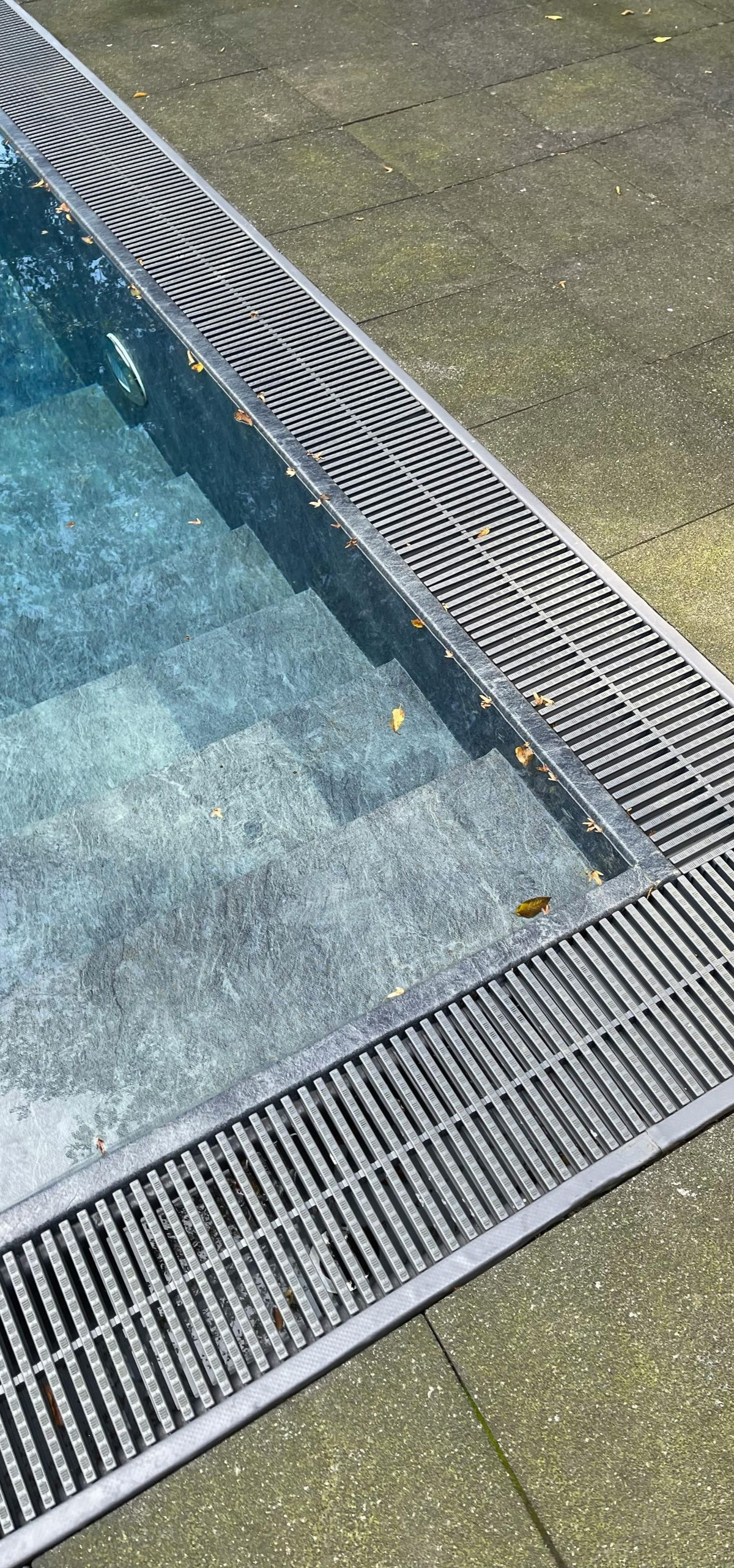 Pool corner with blue water and silver metal grate drainage along the edge