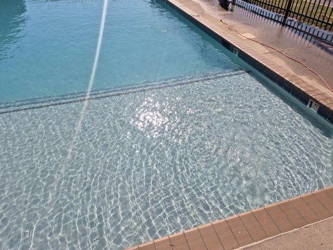 Sunlit swimming pool with rippling blue water and tan tile deck along the edge