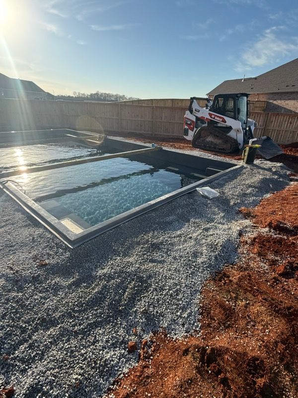 Backyard with a newly installed in-ground pool, gravel edging, and a compact machine near a house.