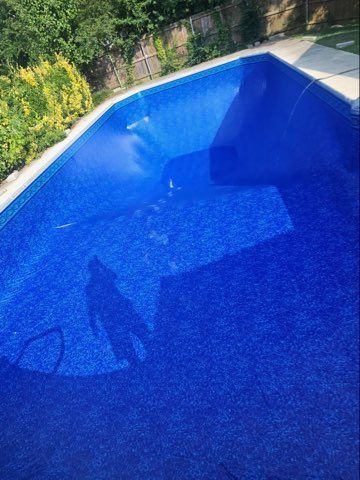 Blue swimming pool with a shadow of a person holding a hose on the water surface