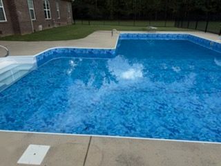 Blue backyard swimming pool with a concrete deck and a small white diving board area
