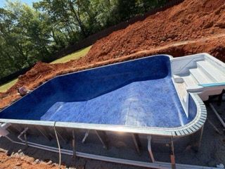 Empty in-ground swimming pool under construction with blue liner and surrounding dirt excavation