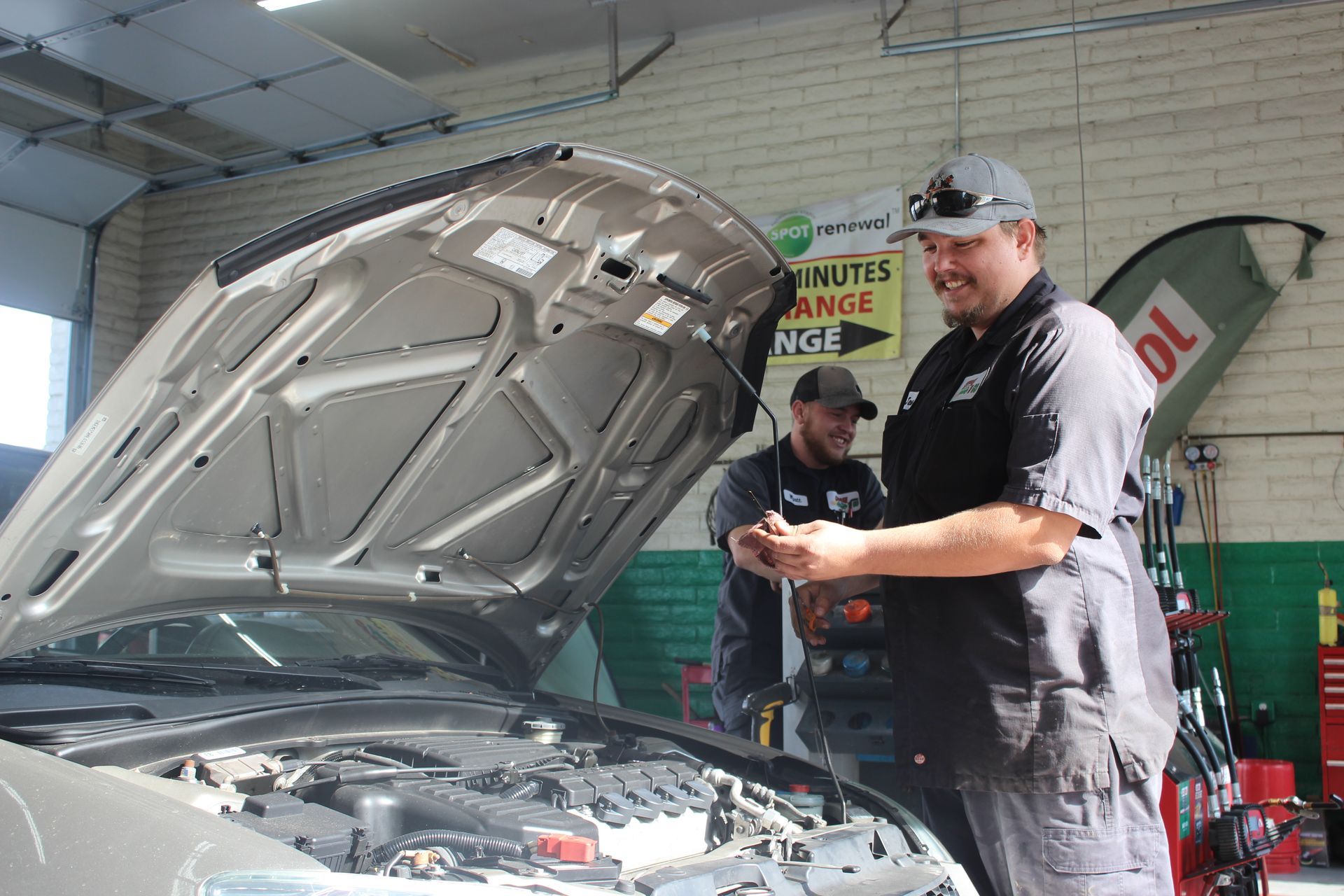 Two men are working on a car in a garage with the hood up.