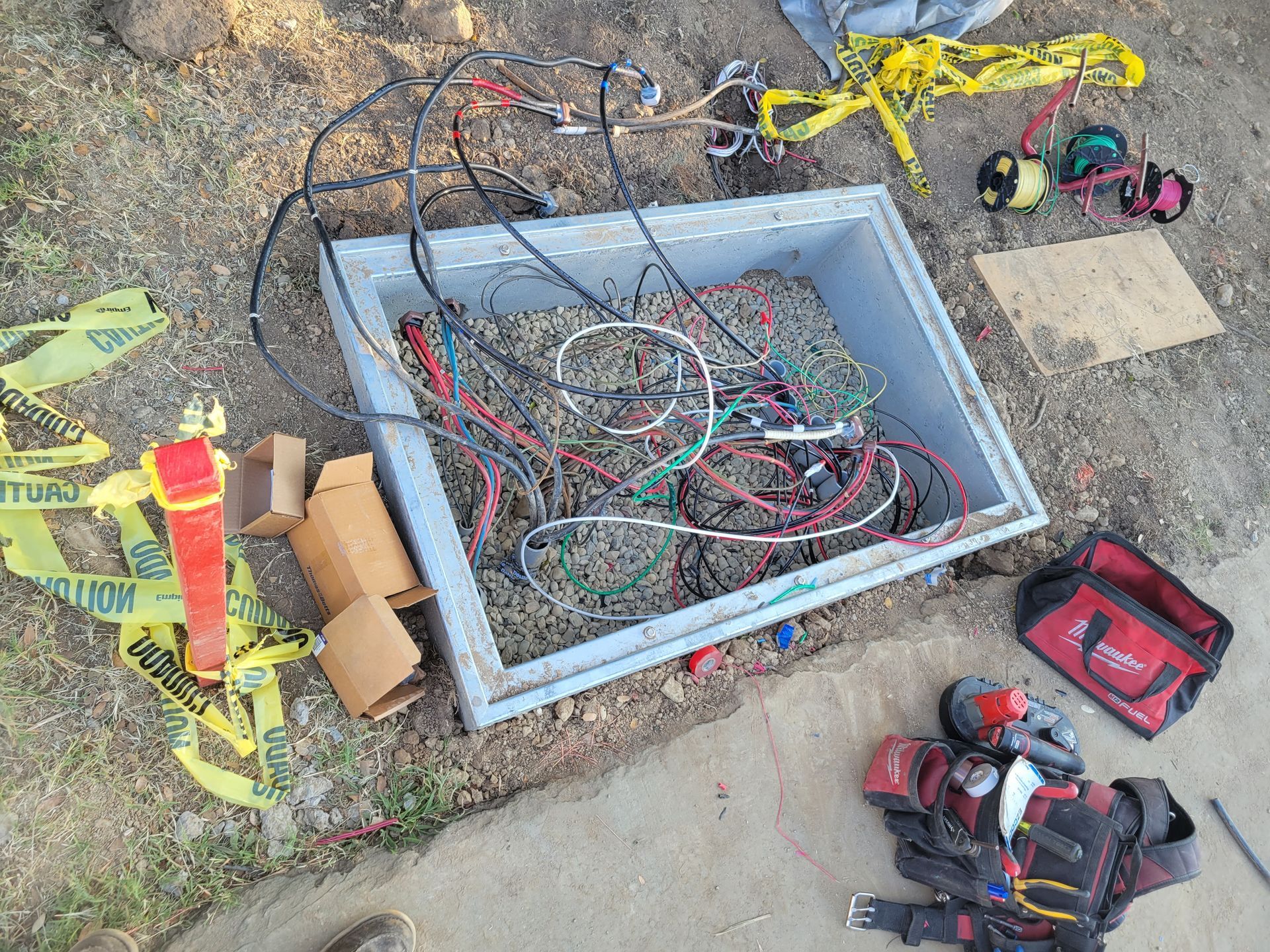 Wiring and tools scattered around an open utility box beside a sidewalk.