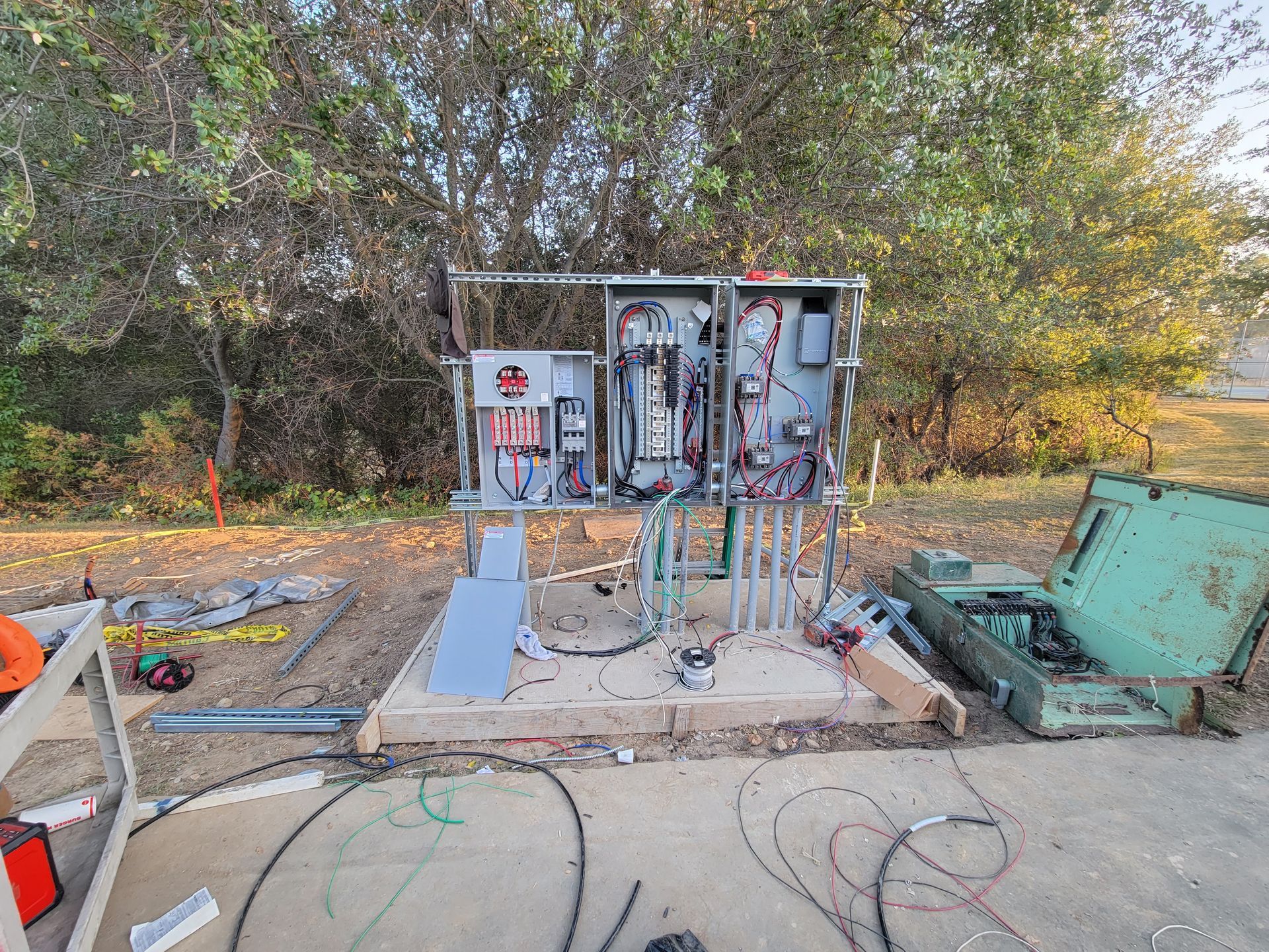 Electrical equipment and cabinets set up outdoors on a concrete pad near trees and a green utility box